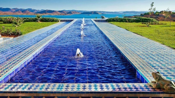 Una piscina larga y estrecha con un diseño de mosaicos a cuadros y una fuente central.