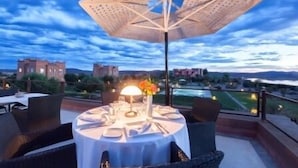 Mesa dispuesta al aire libre con mantel, lámpara y arreglo floral.