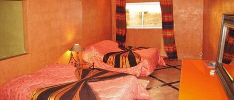 Una habitación con dos camas, una mesita, una lámpara y un ventanal con cortinas.