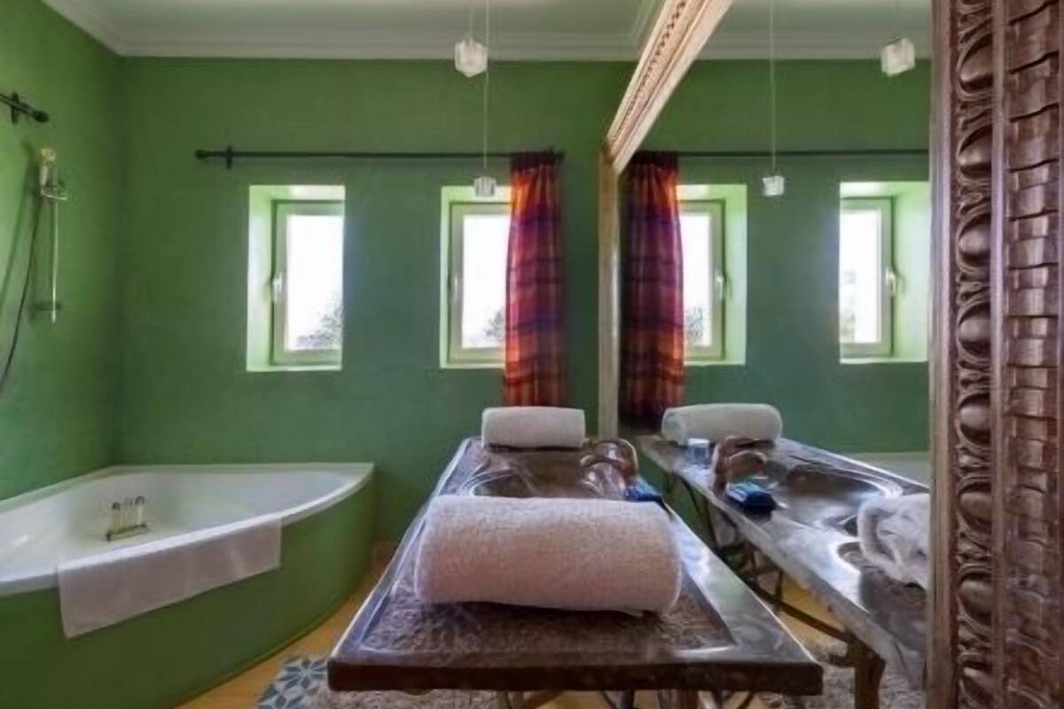 Ein Zimmer mit einer großen Badewanne, einer Massageliege und zwei mit Vorhängen versehenen Fenstern.