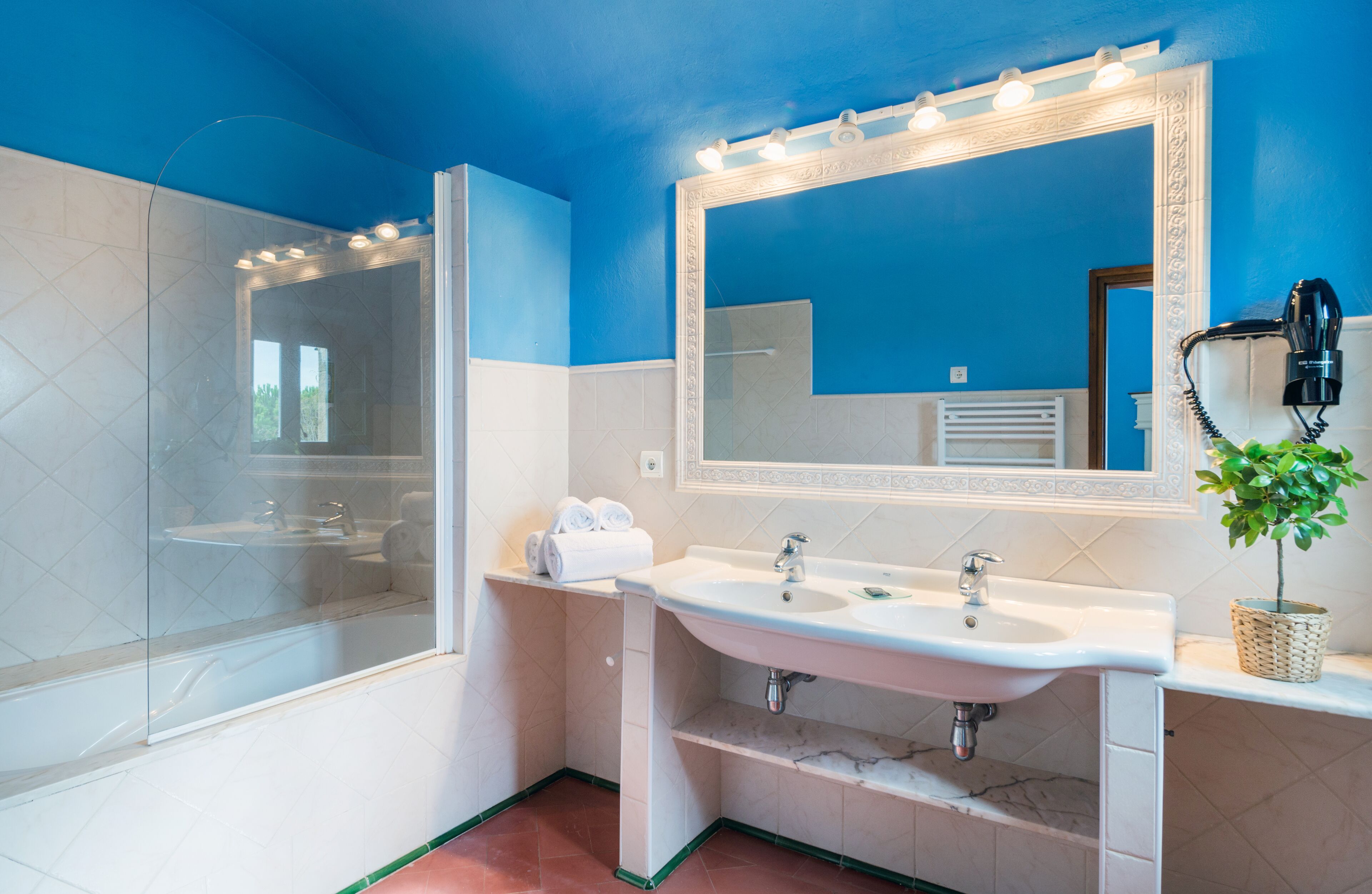 Un baño con cabina de ducha de vidrio, lavabo con espejo y secador de pelo en la pared.