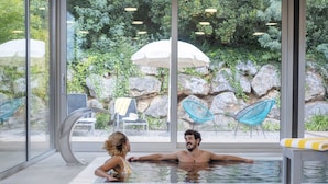 A glass-enclosed indoor swimming pool with a view of a rocky garden and outdoor seating. - Mas Ses Vinyes - Adults Only (Begur)