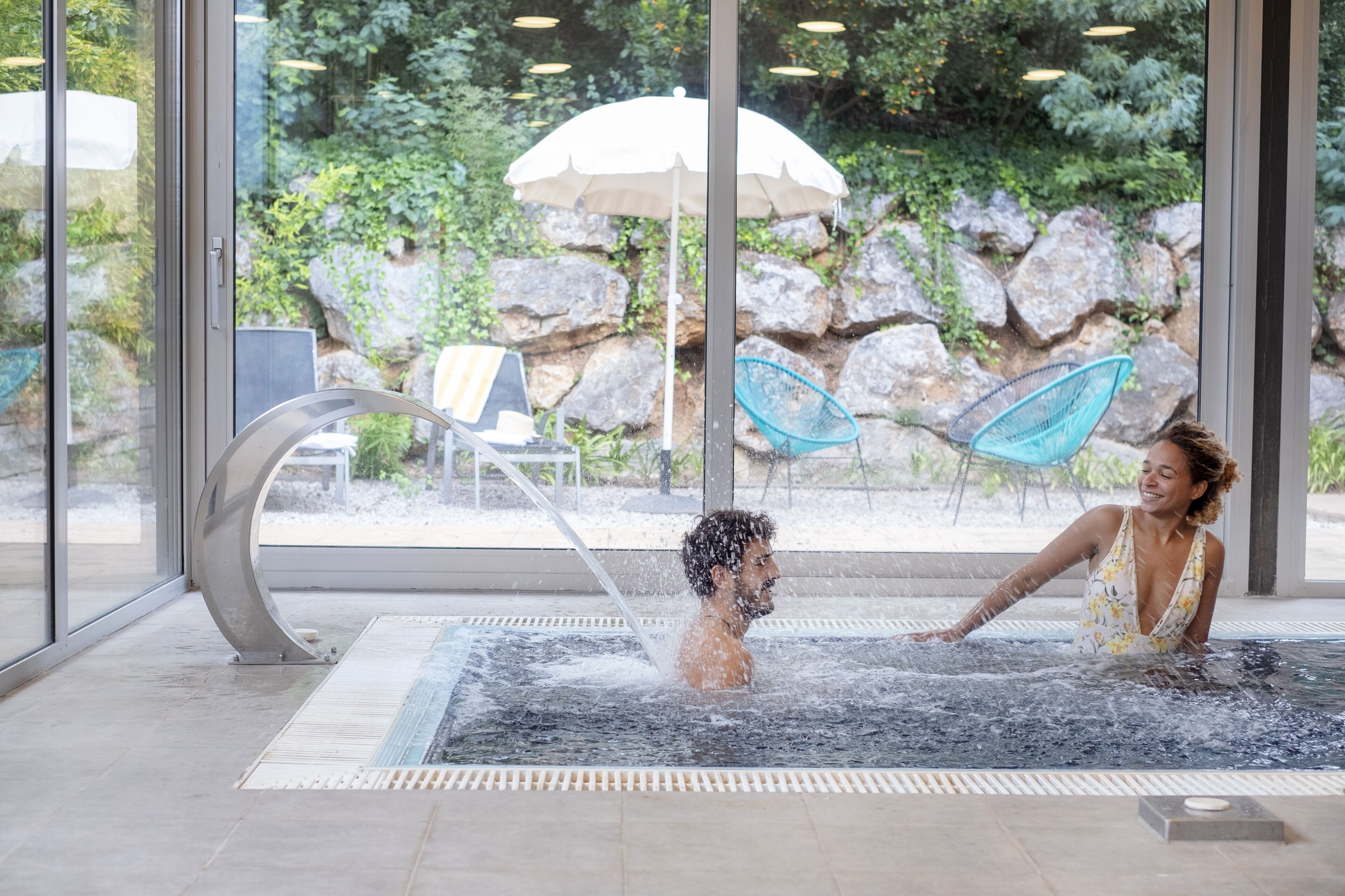 A spa area with a hot tub, a glass wall, and a view of outdoor greenery.