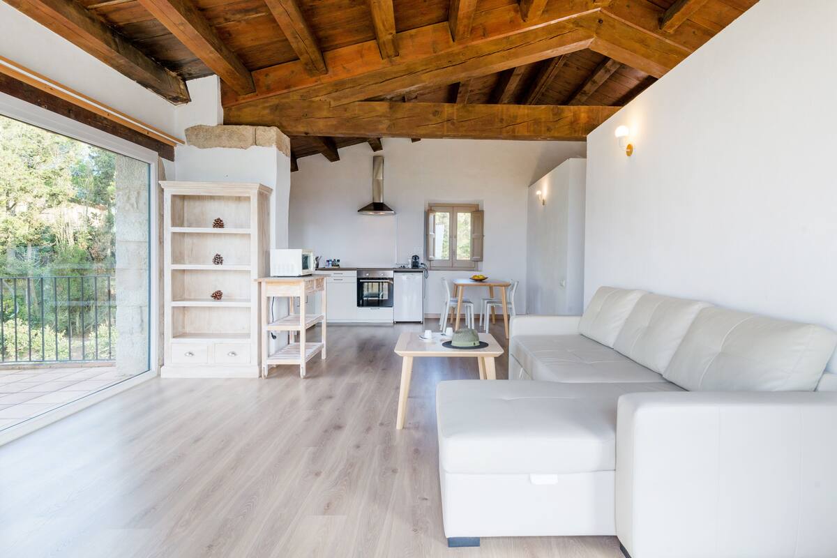 Un vaste espace de vie avec un canapé blanc, un plancher en bois et une cuisine à l’arrière-plan.