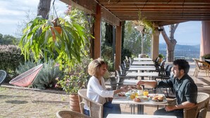 An outdoor patio with wicker furniture, a hanging plant, and a table with breakfast items. - Mas Ses Vinyes - Adults Only (Begur)