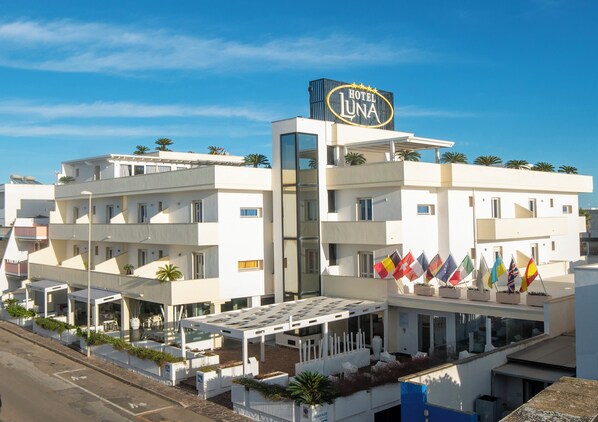 A modern hotel with a prominent sign reading "Hotel Luna," featuring multiple balconies and a series of flags.