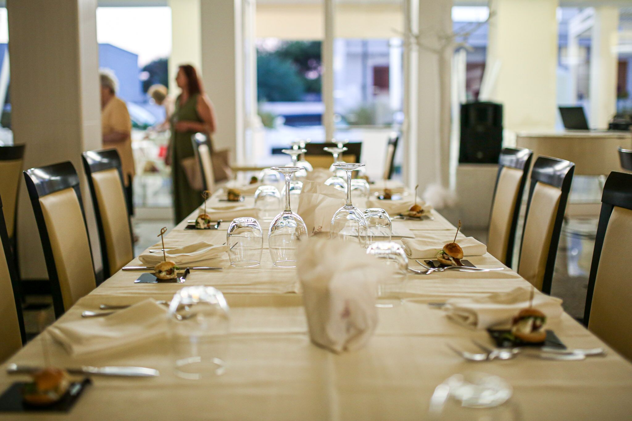 Una larga mesa de comedor con sillas, copas de vino y platos con comida.