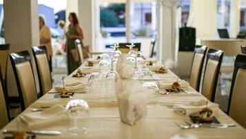 Una larga mesa de comedor con sillas, copas de vino y platos con comida.