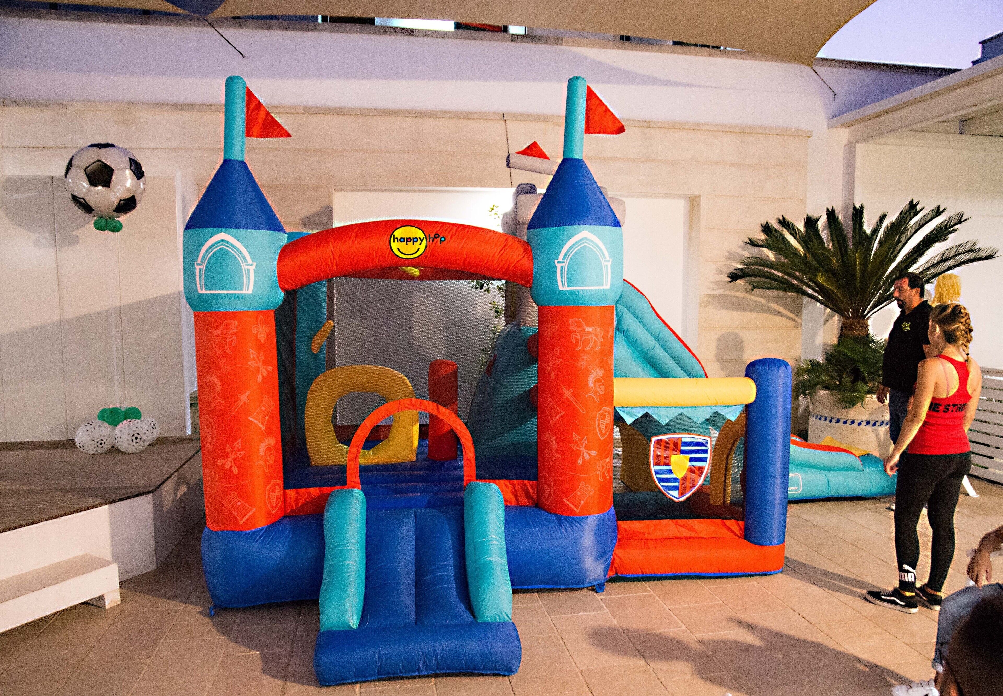 Una estructura inflable y colorida con diseño de castillo, que incluye un tobogán y una red para escalar.