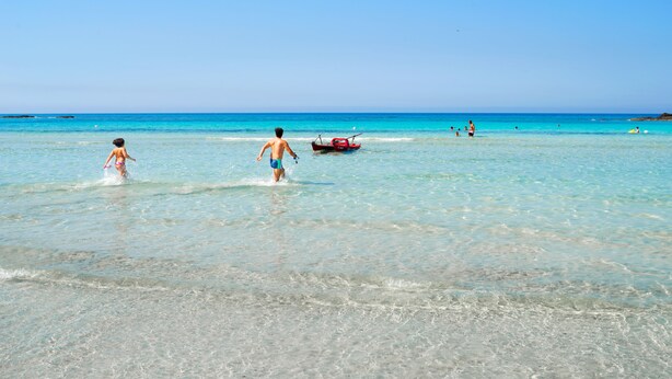 Une plage avec une eau turquoise et limpide, un bateau et des gens qui profitent de la mer.