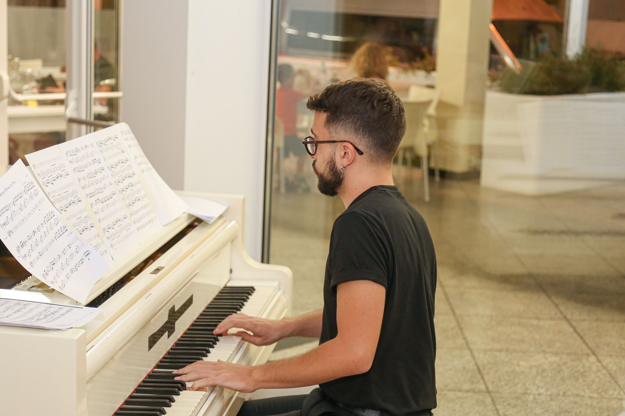 Une personne jouant d’un piano à queue blanc, avec une partition devant elle, dans un décor intérieur moderne.