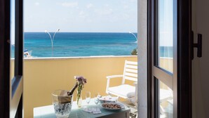 Un balcon avec vue sur l’océan, une table avec une bouteille de champagne, un vase rempli de fleurs et une assiette de collations.