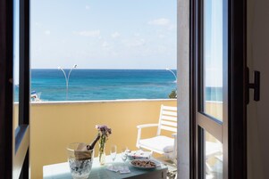 Un balcón con vista al océano, una mesa con una botella de champán, un florero con flores y un plato de aperitivos.