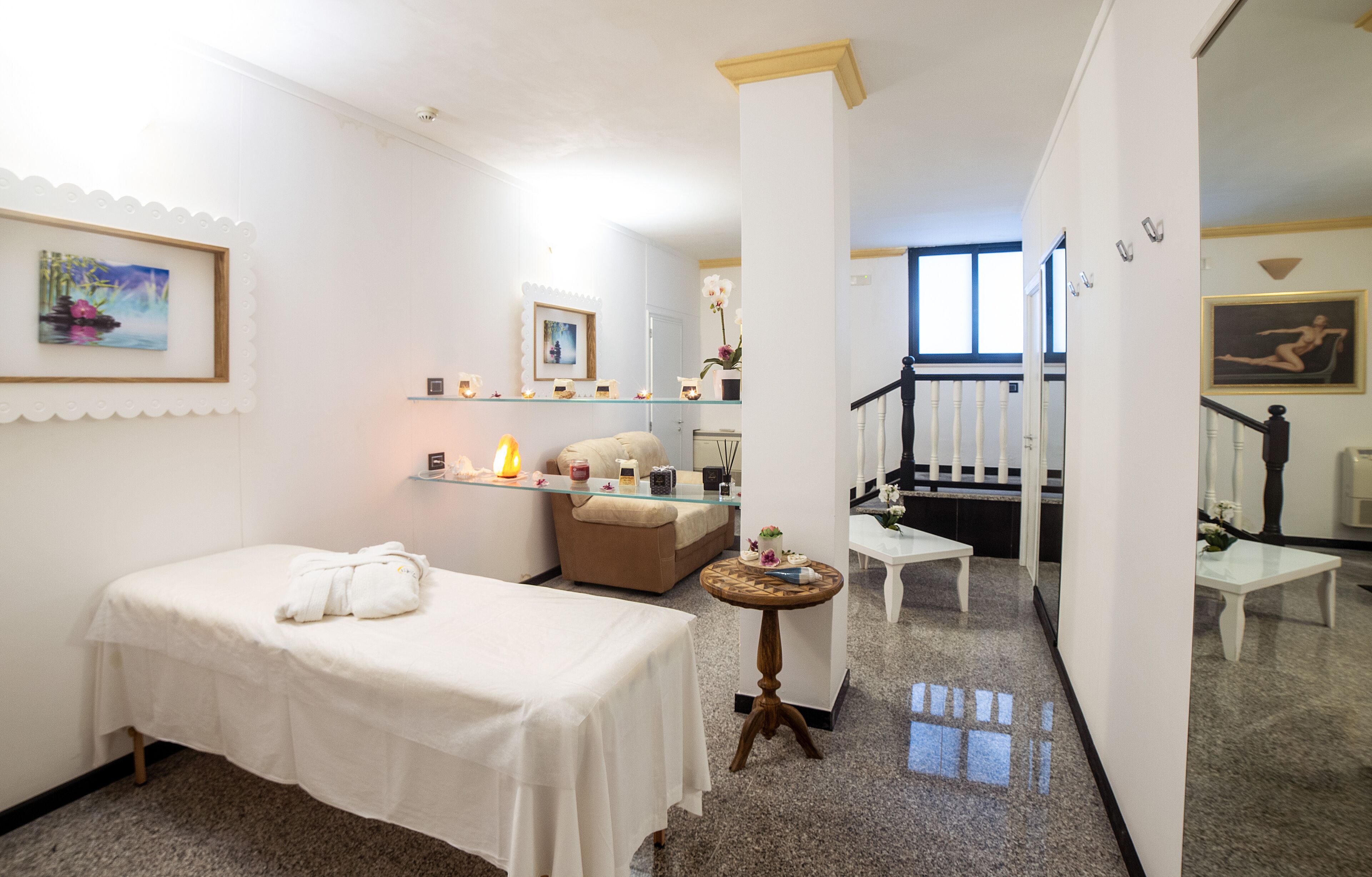 Ein Spa-Raum mit Massageliege, einem kleinen runden Tisch mit Kerzen, einer Bank und einer Treppe zu einem weiteren Bereich.
