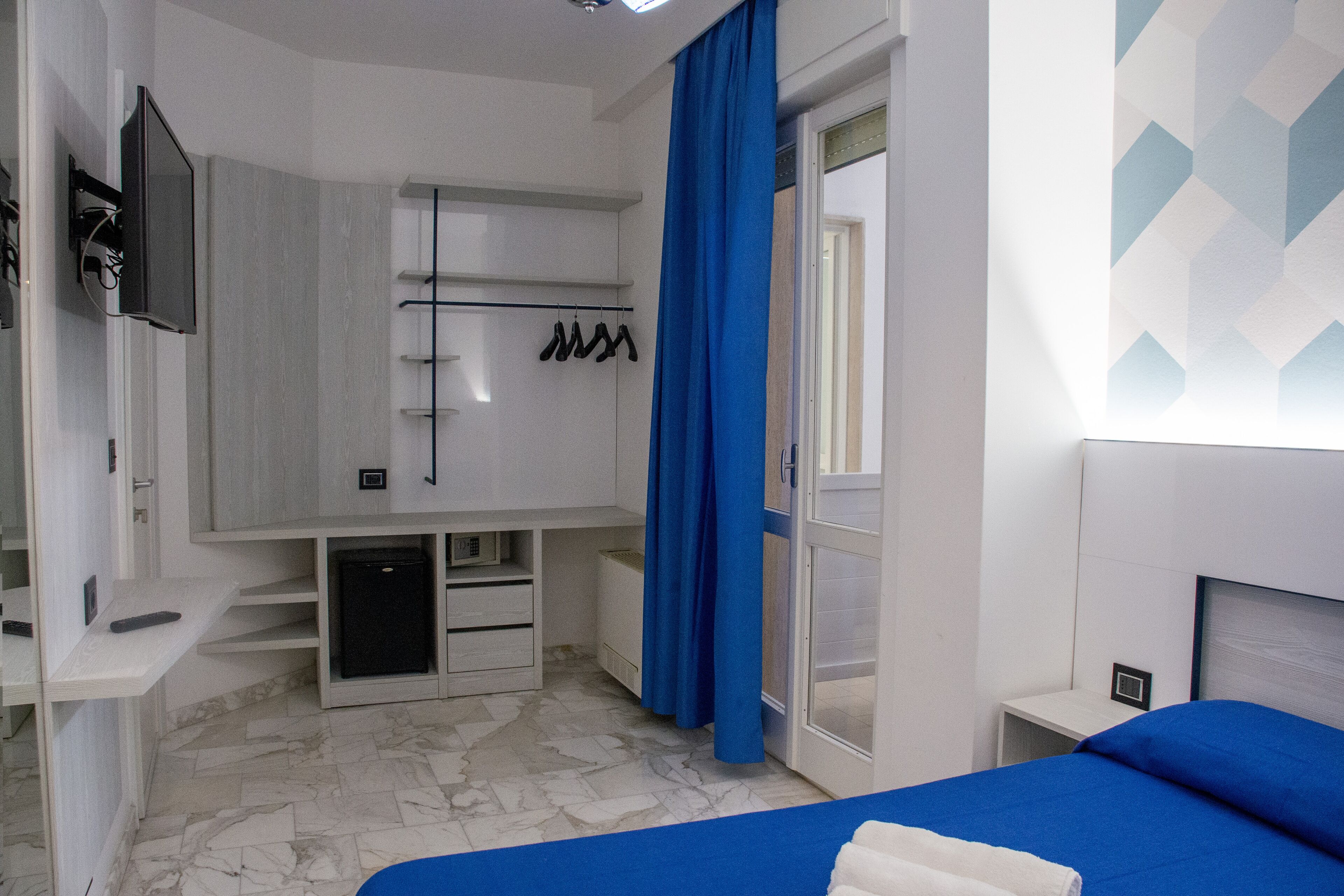 Un dormitorio con cama, televisor, armario y un pequeño escritorio.