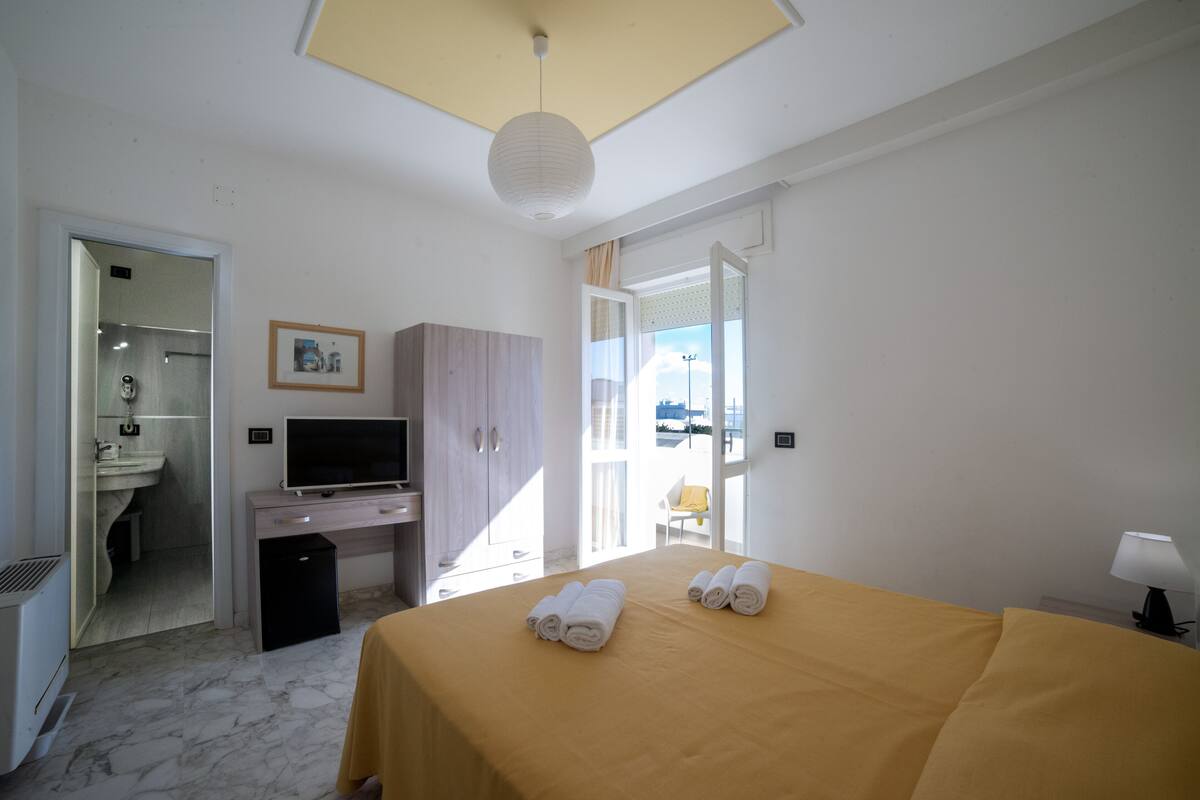 A hotel room with a bed, a desk, a television, and a bathroom visible through an open door.