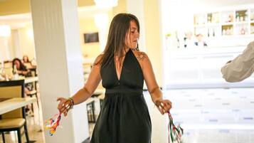 Una mujer con un vestido negro sostiene cintas de colores en un espacio interior bien iluminado con mesas y sillas.