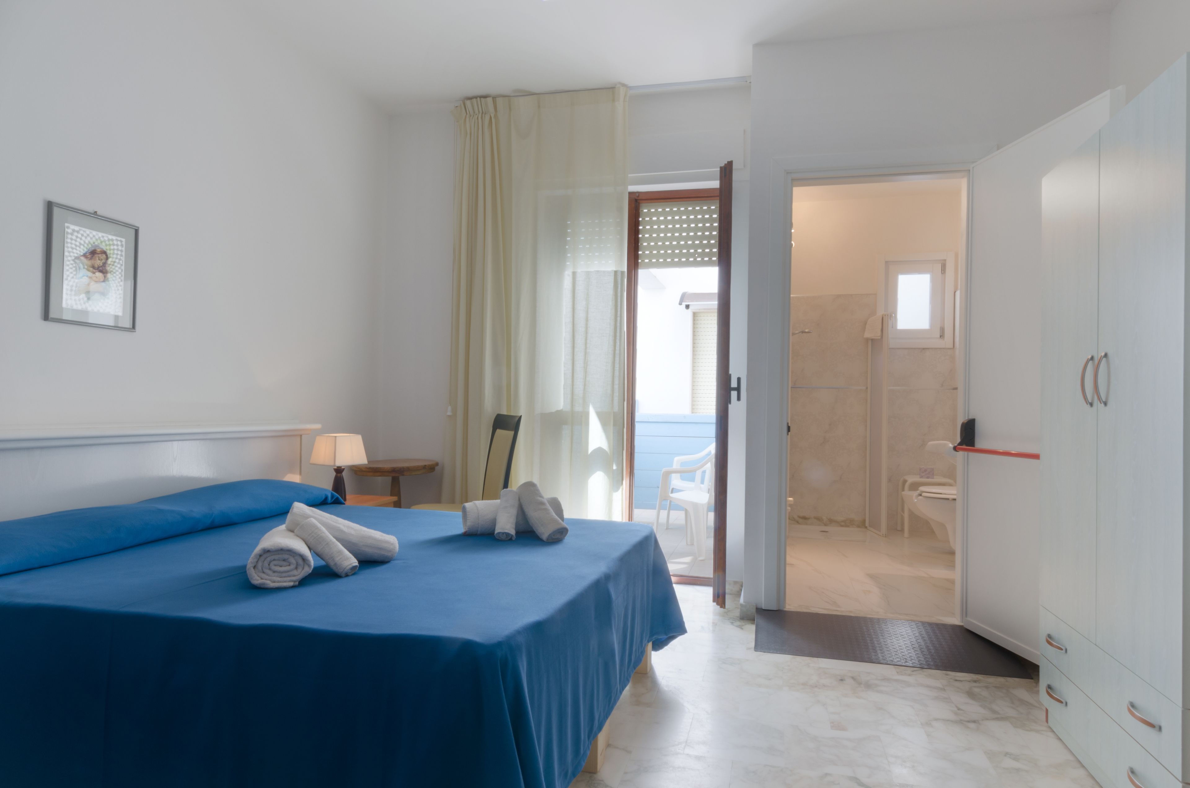 A hotel room with a bed, a nightstand, a framed picture, and a bathroom visible through an open door.