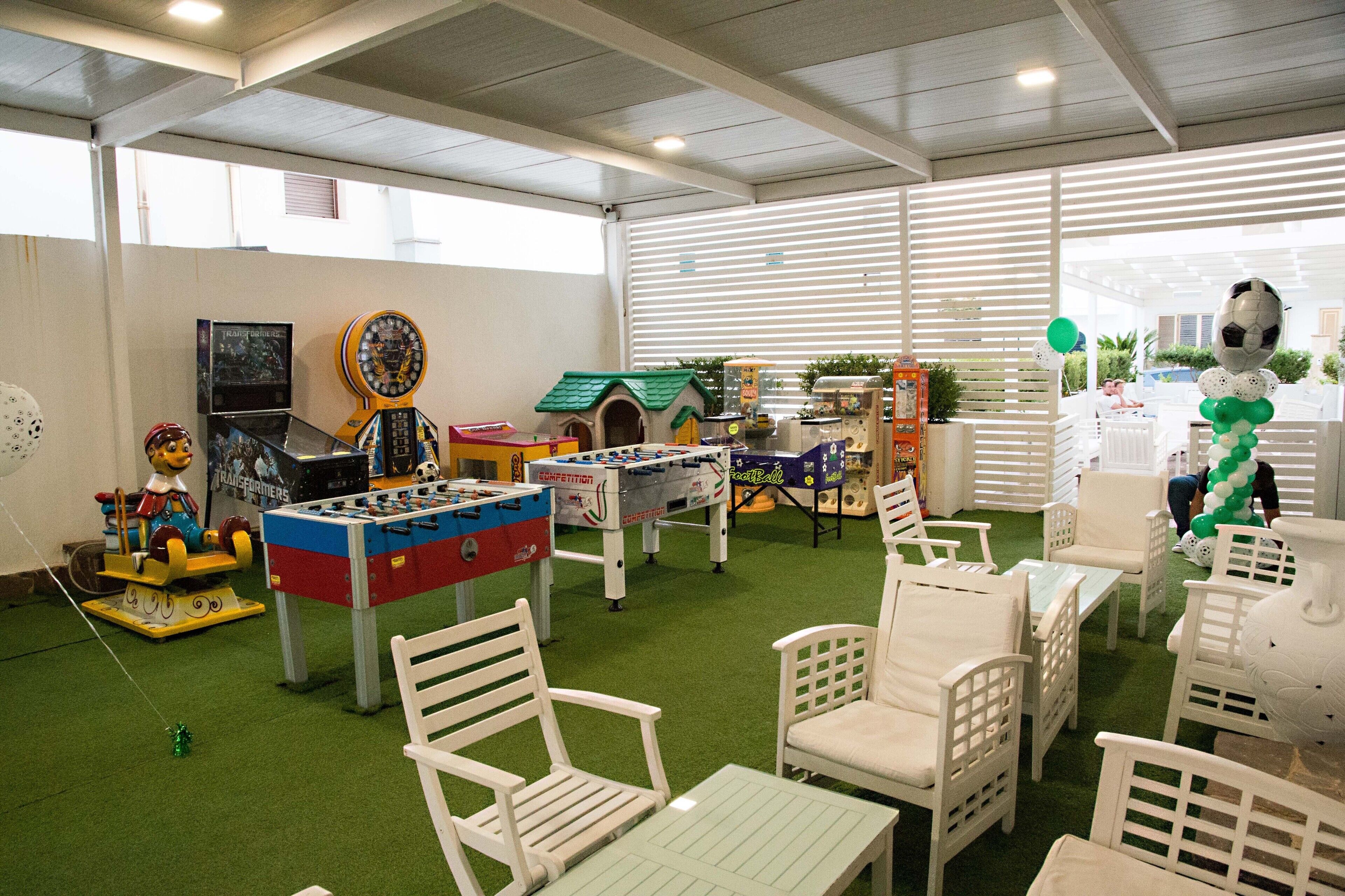Una habitación con césped artificial verde, muebles blancos y diversos juguetes y juegos infantiles.