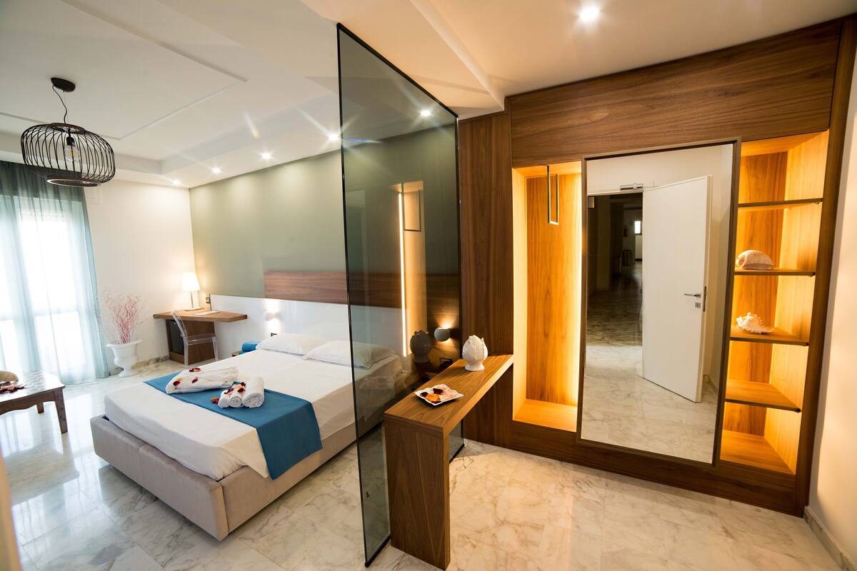 A modern hotel room with a large bed, bedside table, and a mirror with shelves.