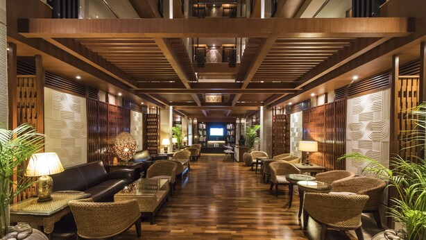 Un vestíbulo de hotel con piso de madera, sofás de cuero, sillones de mimbre y un televisor en el centro.