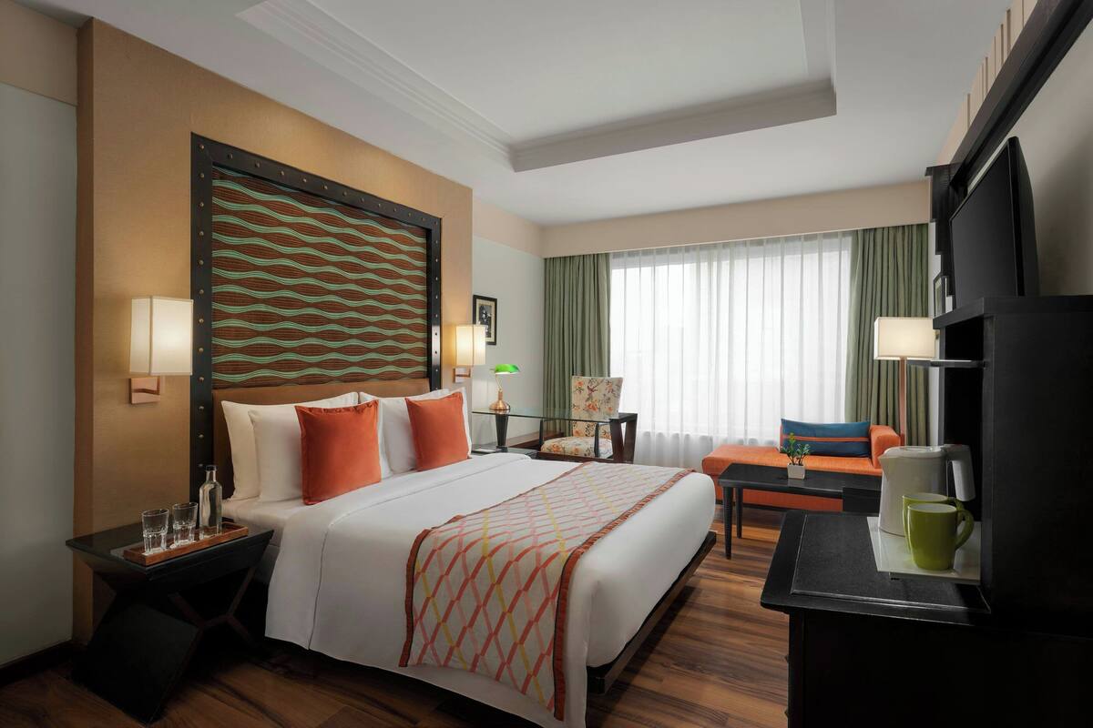 Habitación de hotel con una cama grande, un escritorio, una silla, un televisor y una ventana con cortinas.