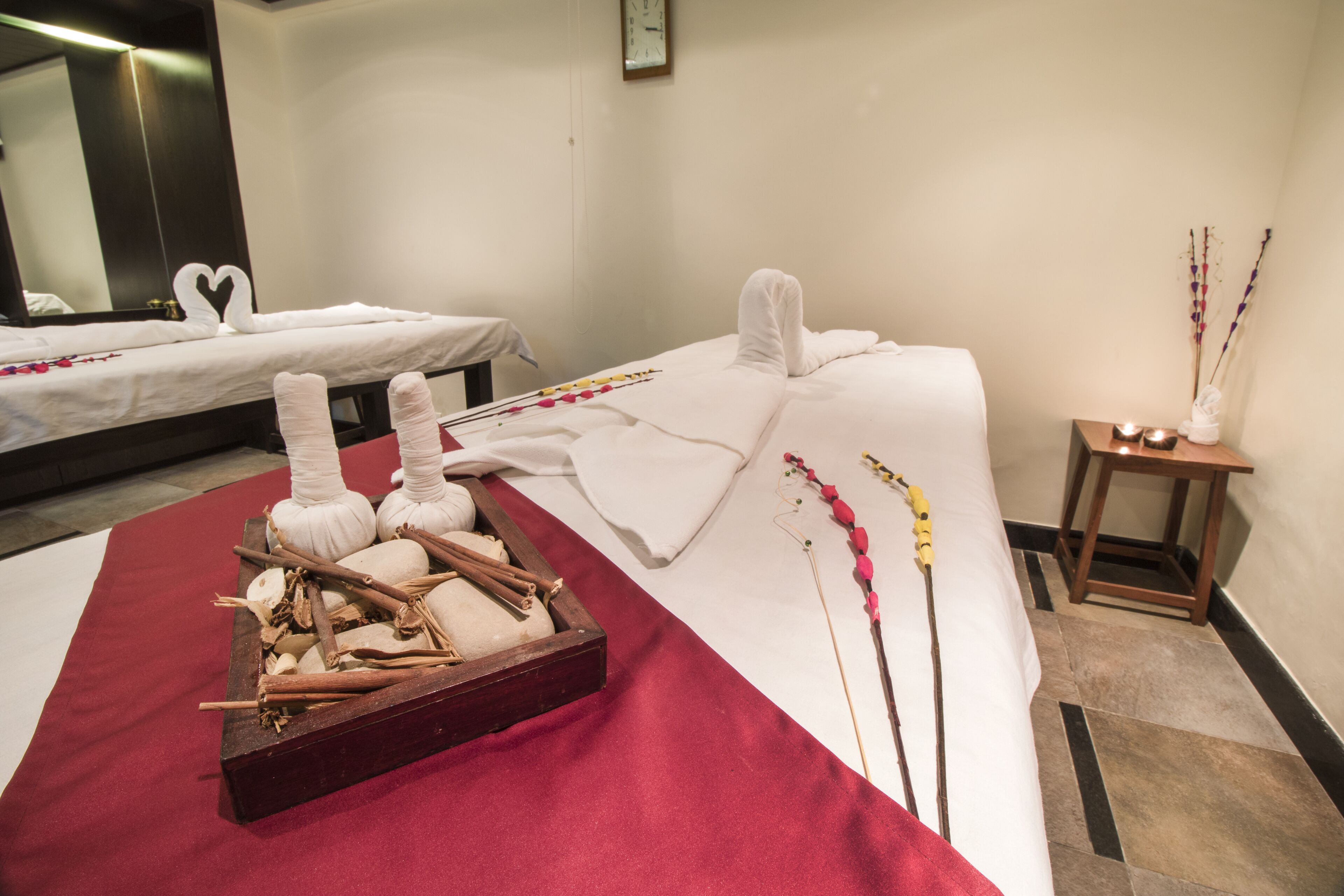 Ein Wellnessraum mit zwei Betten, einem Holftablett mit natürlichen Elementen und einem kleinen Tisch mit Kerzen.