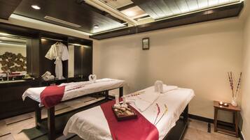 Relax in a serene spa room with two massage tables, a candlelit side table, and a decorative mirror.