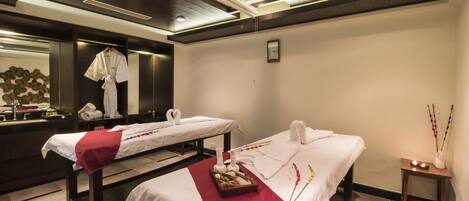 A spa room with two beds, a mirror, a sink, and a small table with candles and flowers.