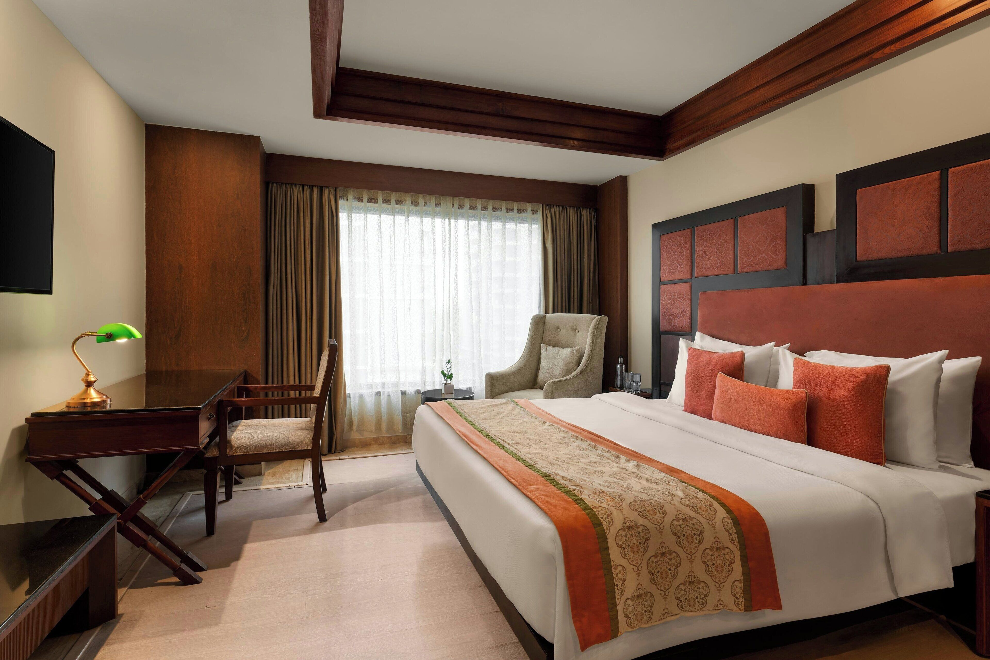 Habitación de hotel con cama, escritorio, silla, televisor y ventana con cortinas.