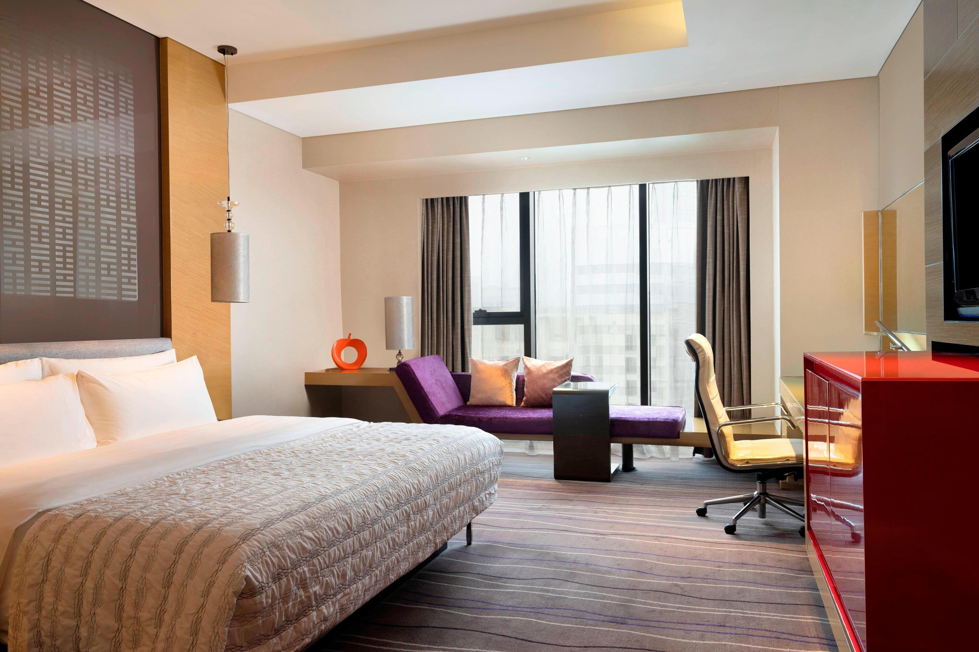 A hotel room with a large bed, a desk with a chair, a sofa, and a TV.