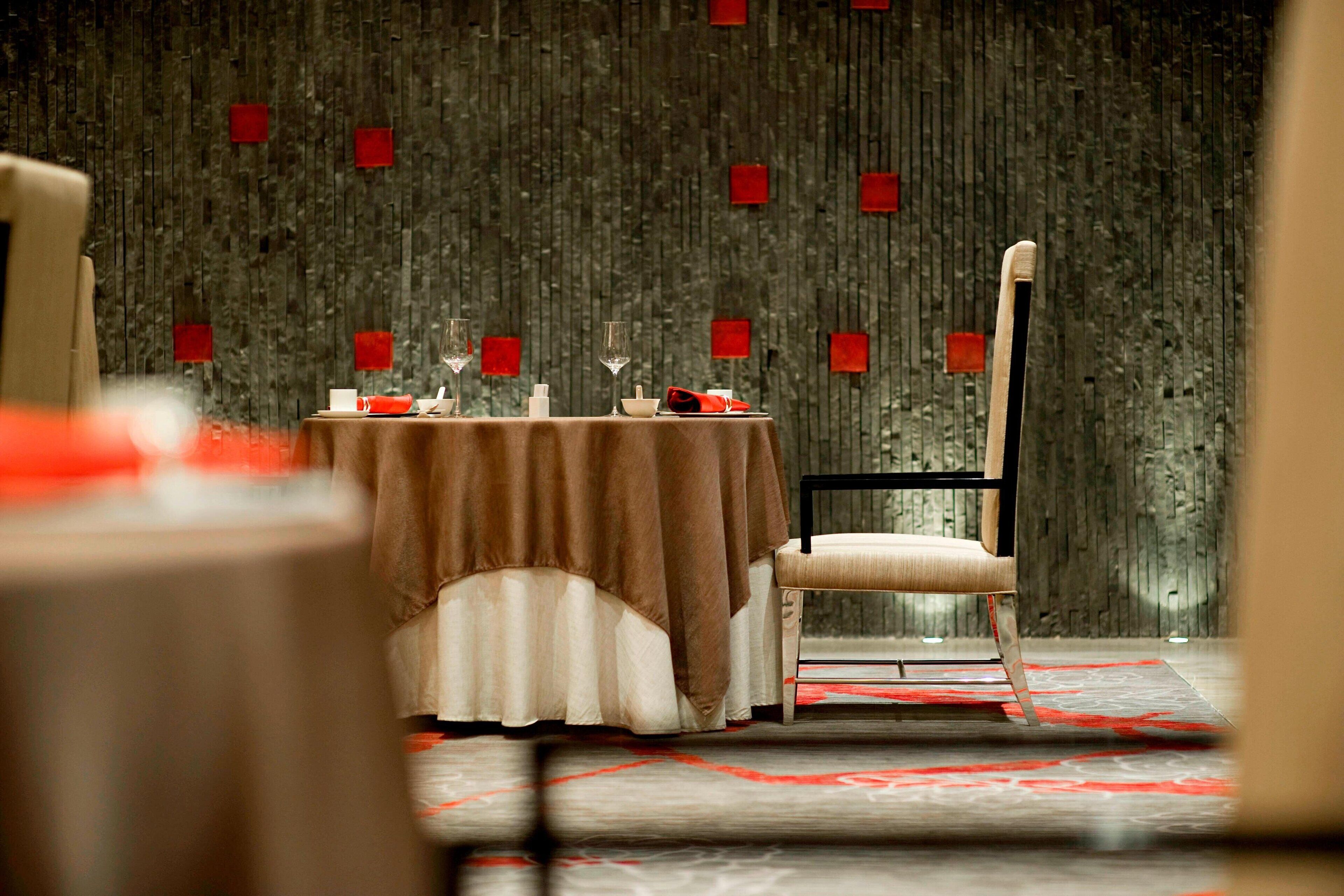 A dining area with a table set for two, a chair, and a patterned carpet.