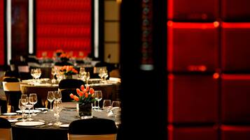 A dining area with tables set for a meal, featuring a vase of orange tulips and wine glasses.