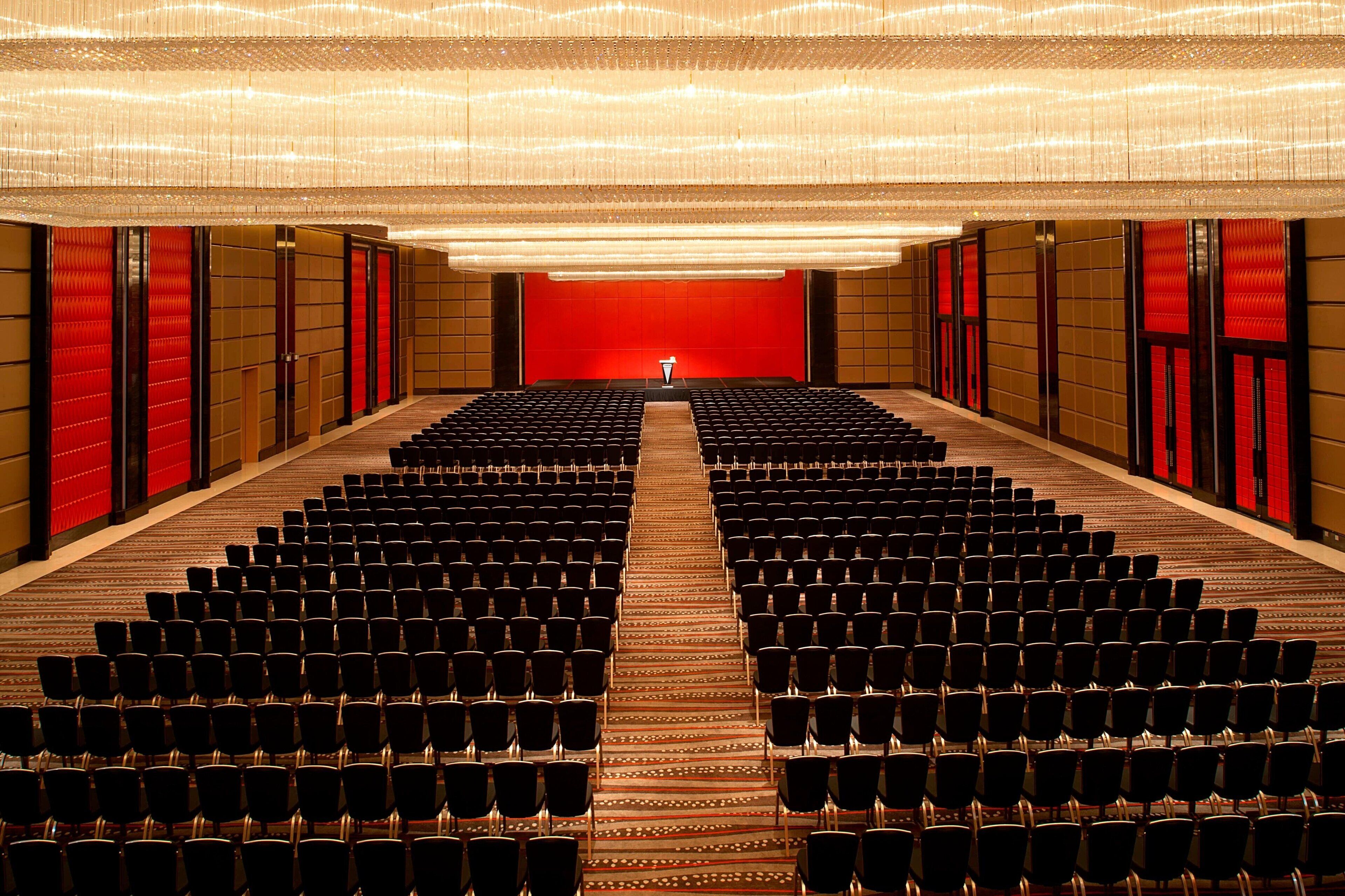 Un teatro con hileras de asientos negros, un escenario rojo y una alfombra estampada.