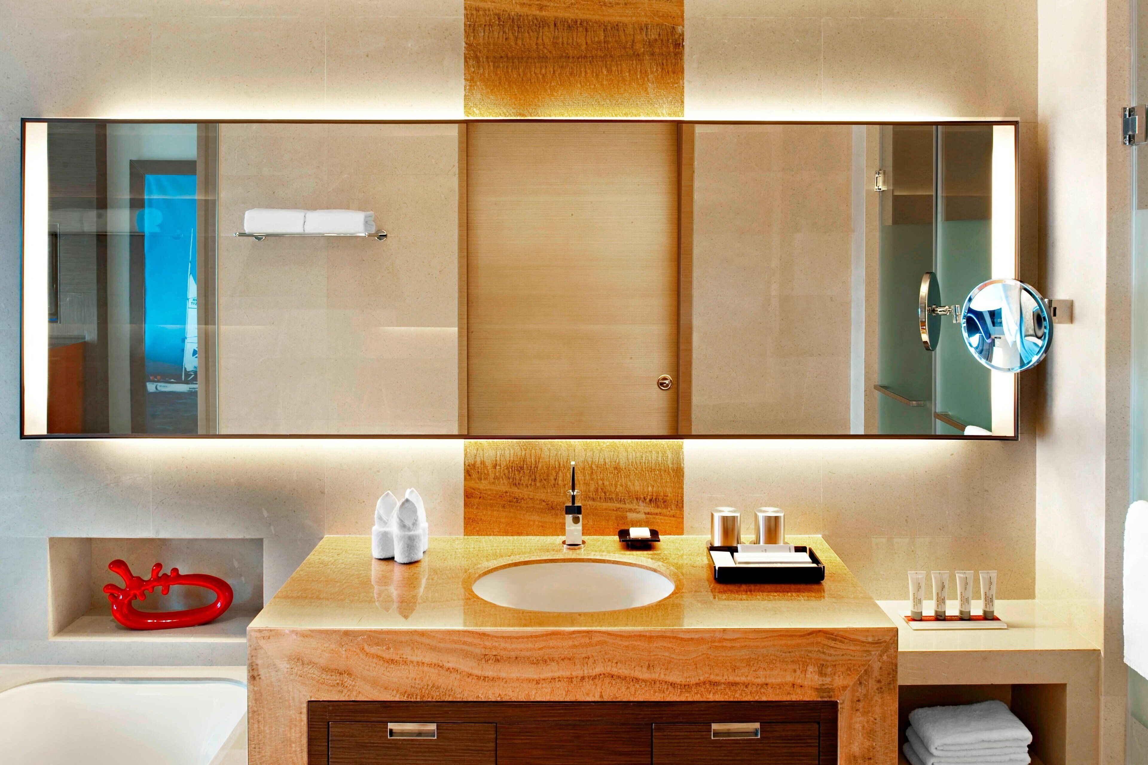 Un baño moderno con un espejo grande, un tocador de madera, un lavamanos y una cabina de ducha de vidrio.