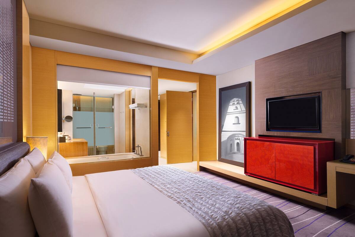 A modern hotel room with a large bed, a television, a red cabinet, and a mirror.