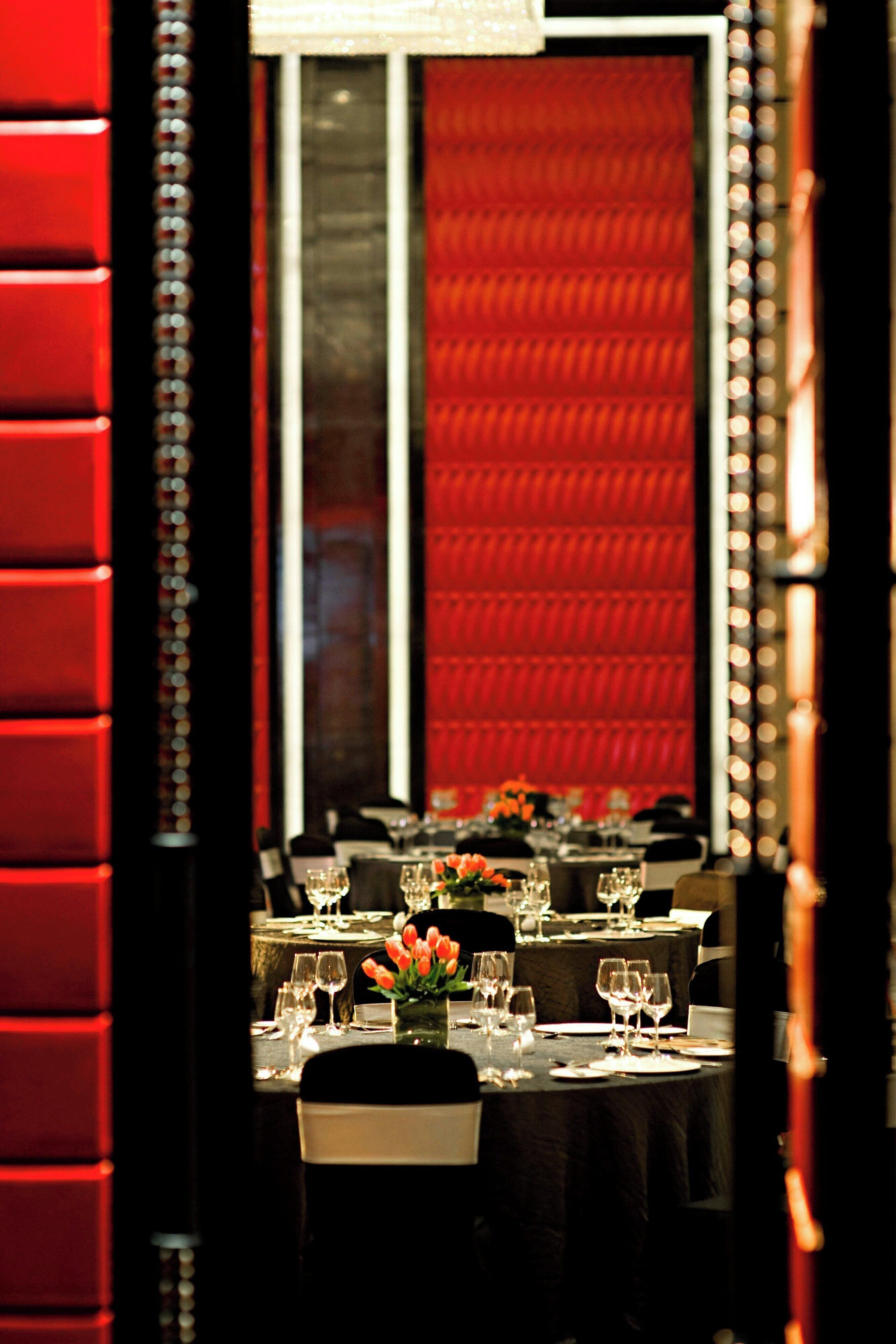 A dining area with tables set for a meal, a mirror reflecting the room, and a red upholstered wall.