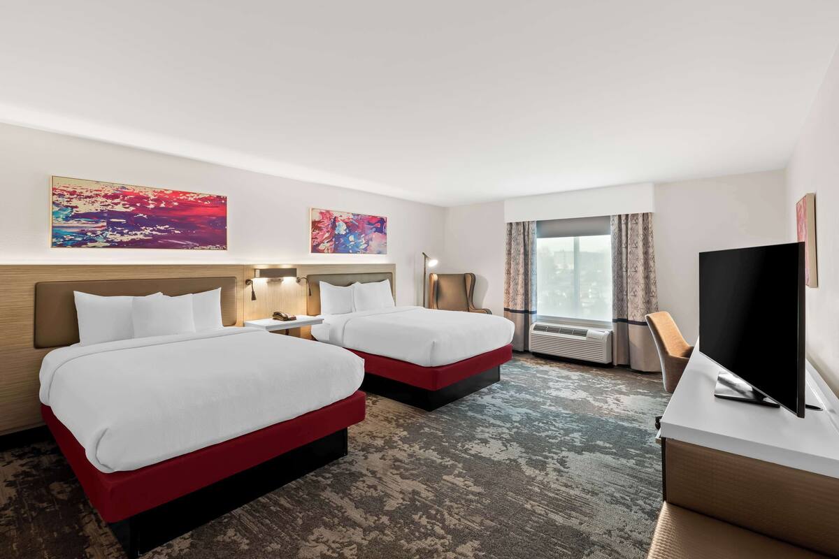 Habitación de hotel con dos camas, un televisor de pantalla plana, un escritorio y obras de arte en las paredes.
