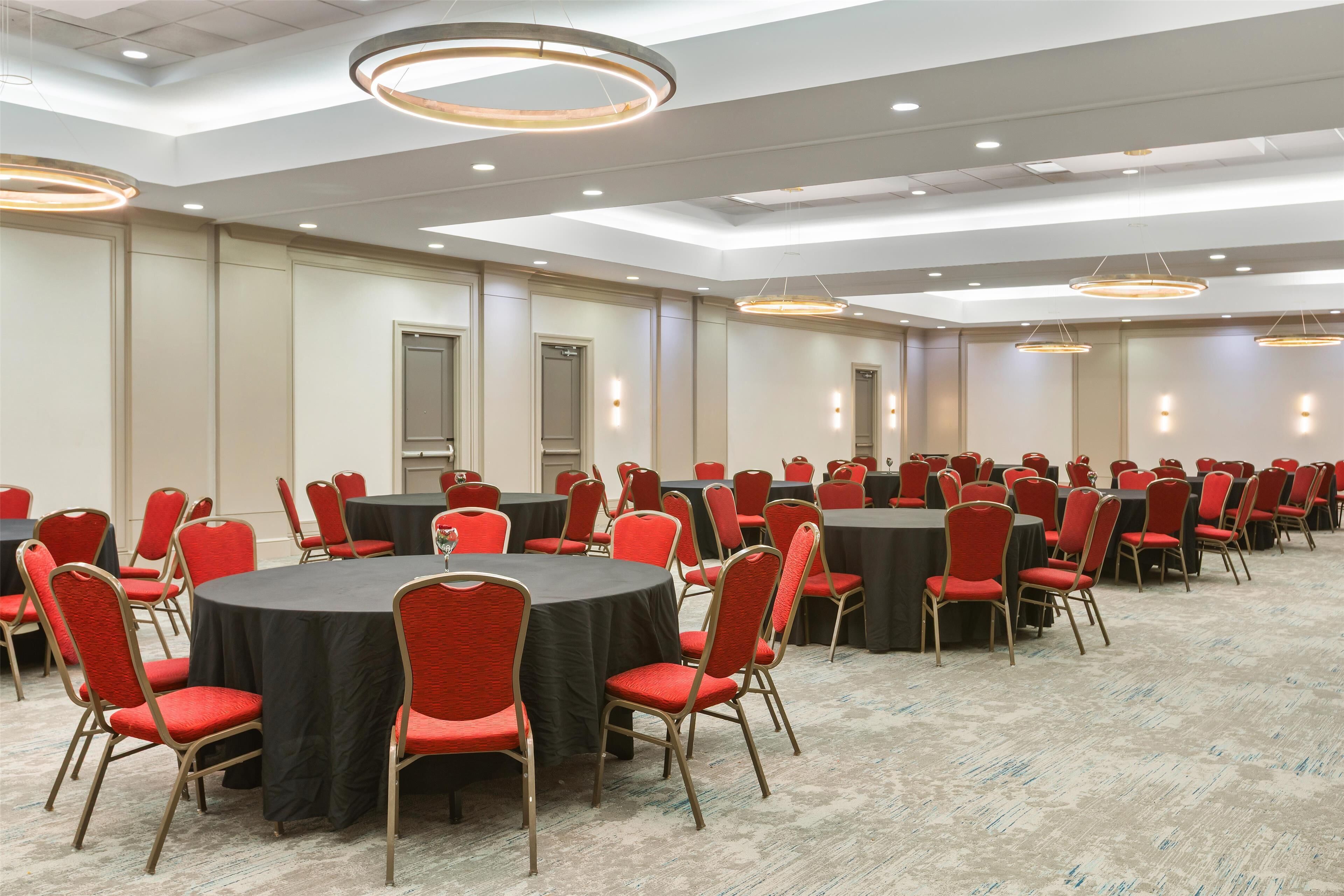 Una sala conferenze con diversi tavoli rotondi, sedie rosse e lampade dal design moderno.