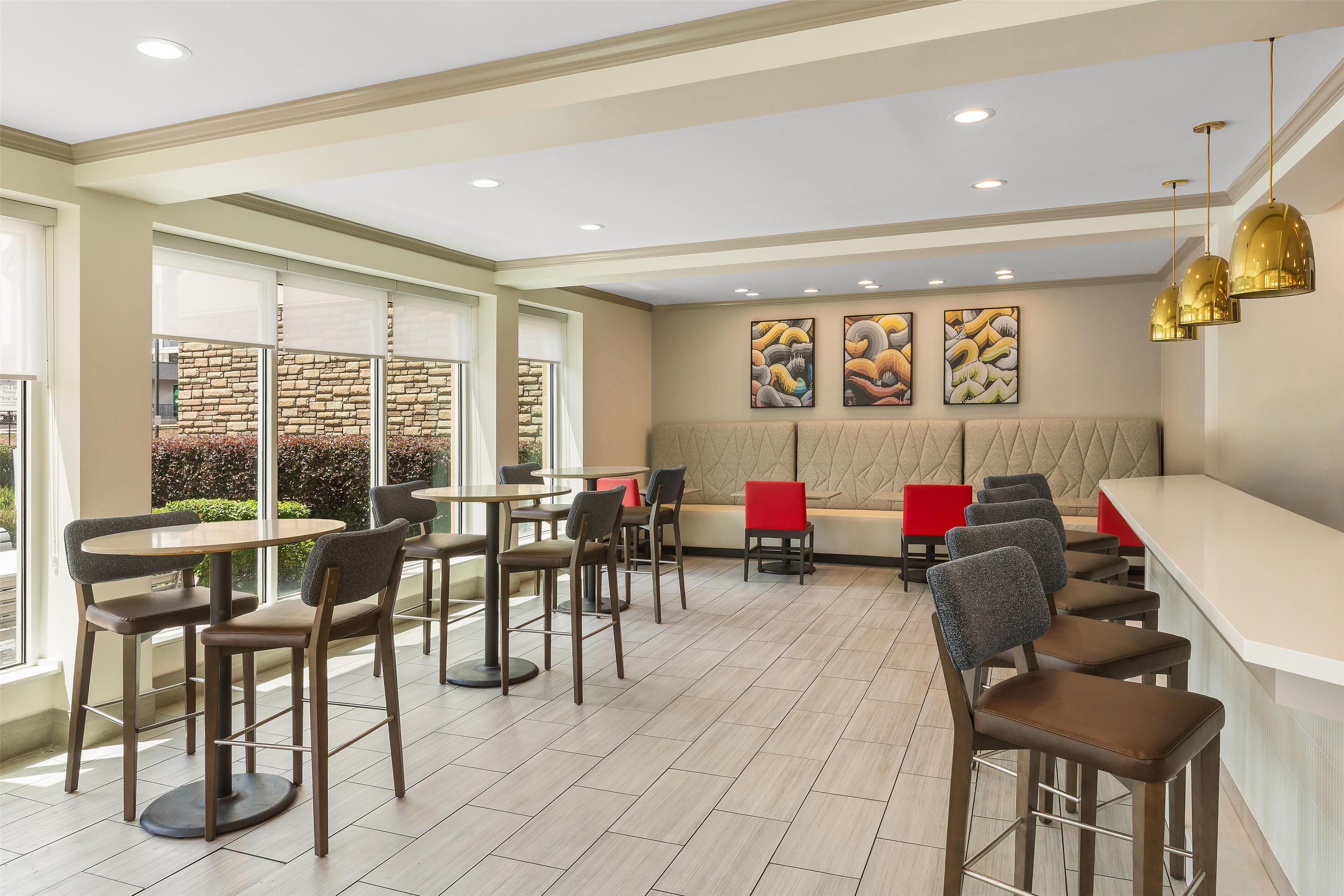 A modern restaurant with high tables and bar stools, a stone wall, and artwork on the wall.