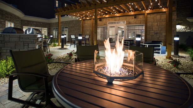 An outdoor patio with a round table, chairs, a fire feature, and a pergola with string lights. - Hilton Garden Inn Atlanta Airport North (Atlanta)