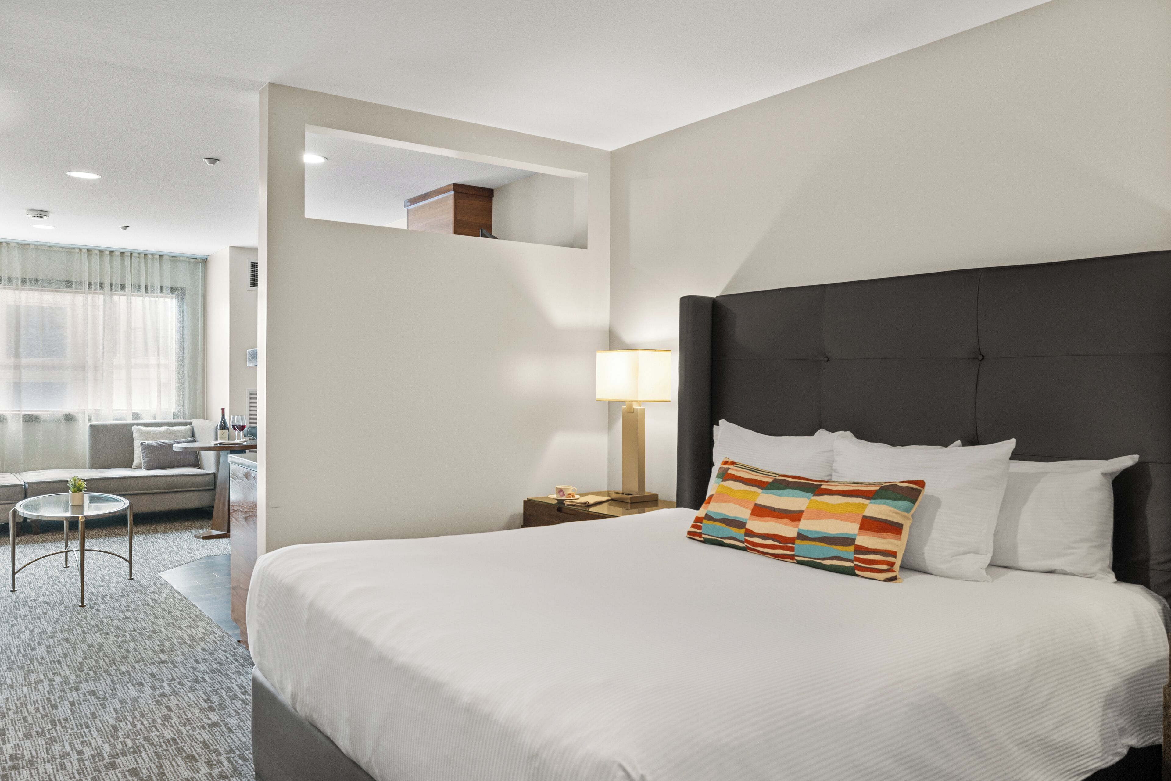 Een hotelkamer met een groot bed, een nachtkastje met lamp, een klein rond tafeltje en een bank.