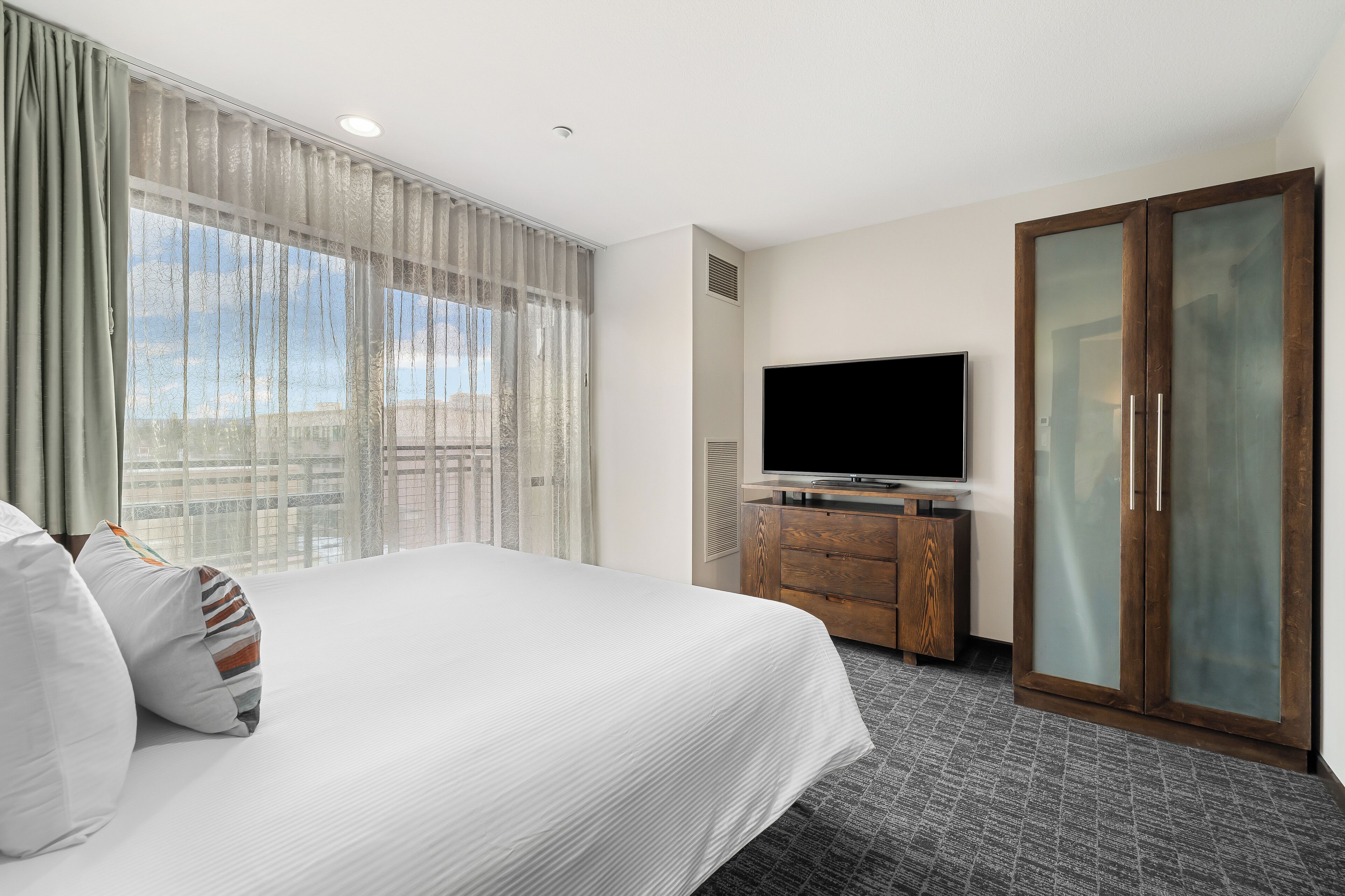A hotel room with a large bed, a flat-screen TV, a wooden dresser, and a sliding glass door.