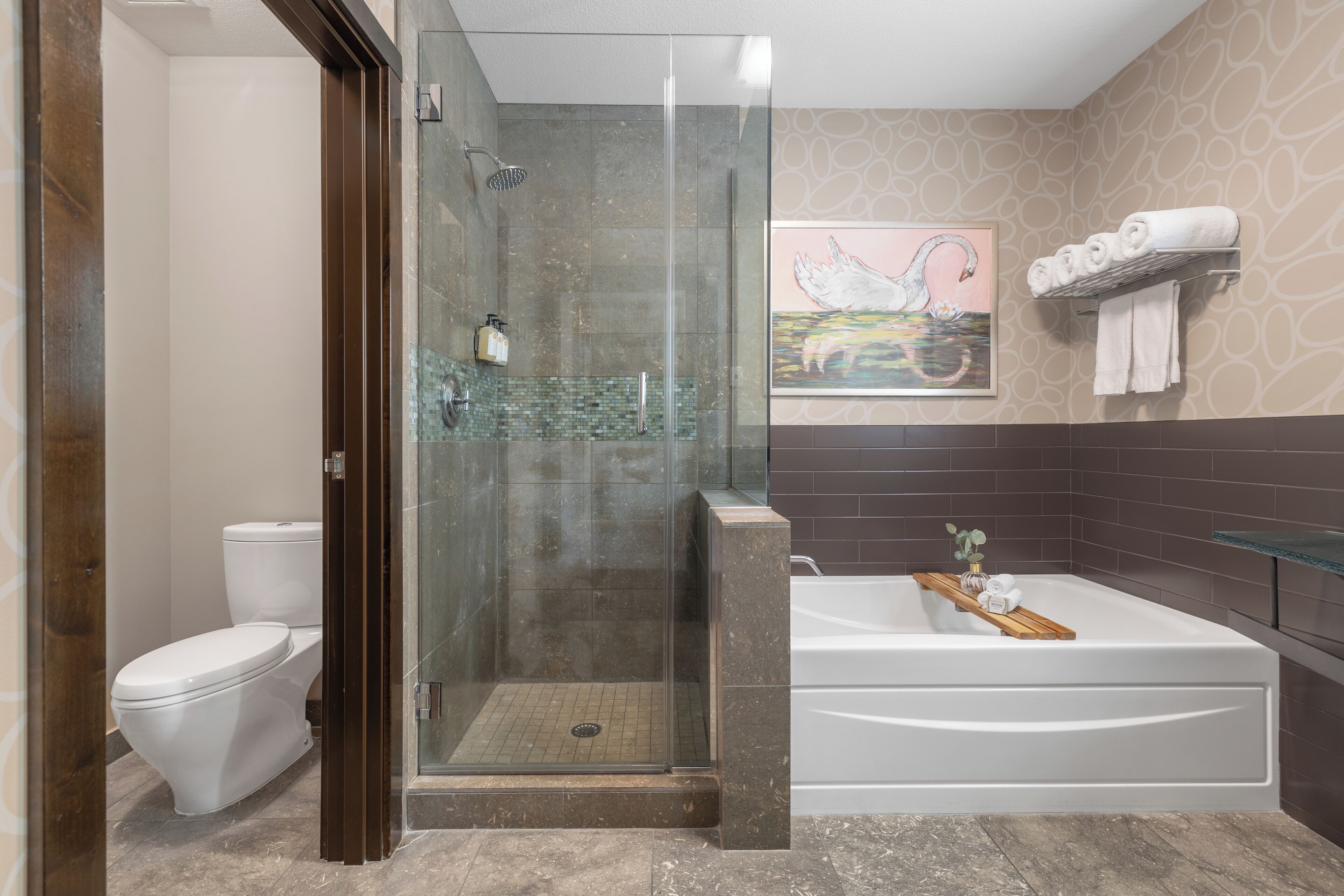 A modern bathroom with a glass-enclosed shower, a white toilet, a bathtub with a wooden tray, and a wall-mounted towel rack.