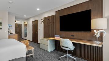 A hotel room with a bed, a desk with a computer, a TV, a lamp, and a chair.