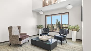 Un vaste salon doté d’un haut plafond, de grandes fenêtres et offrant une vue sur l’extérieur. On y trouve deux fauteuils, un canapé et une table basse.
