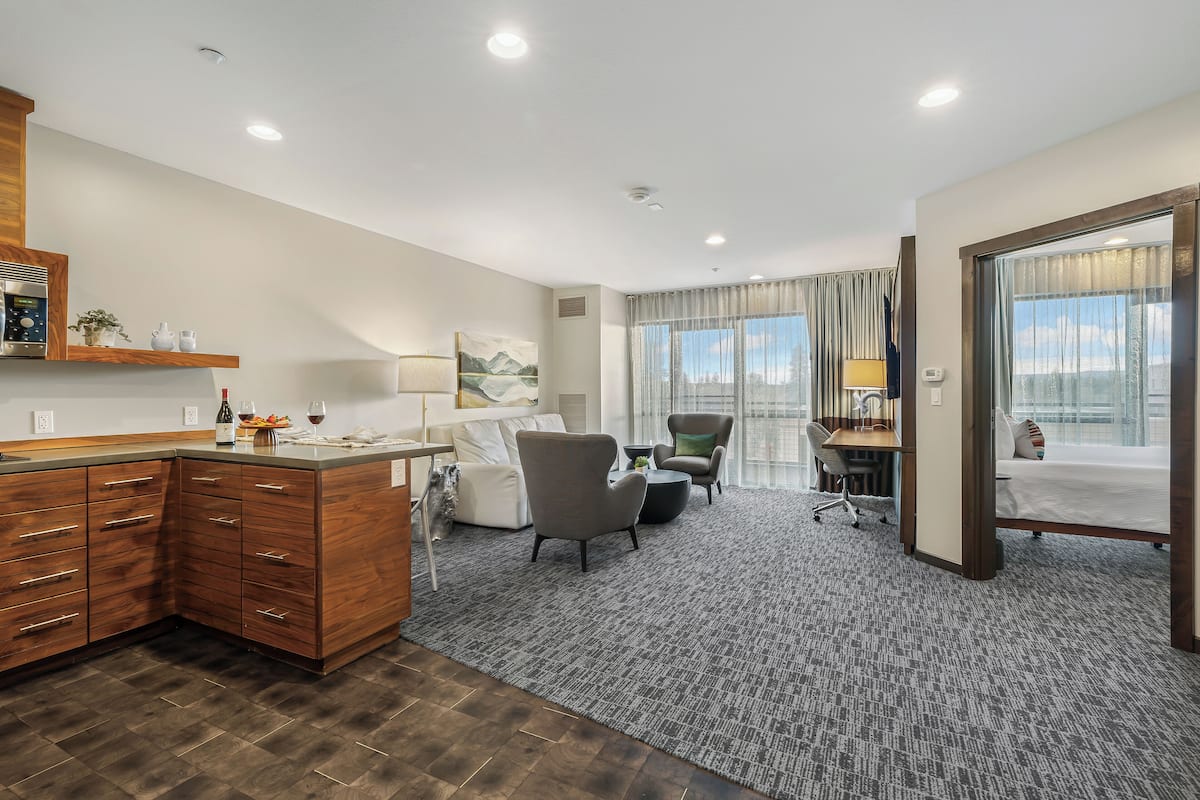 A hotel room with a wooden cabinet, a desk, a chair, a bed, and a large window with curtains.