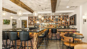 A bar area with a central bar counter, multiple seating options including bar stools and round tables, and a well-stocked liquor display. - The Oxford Hotel Bend (Bend)