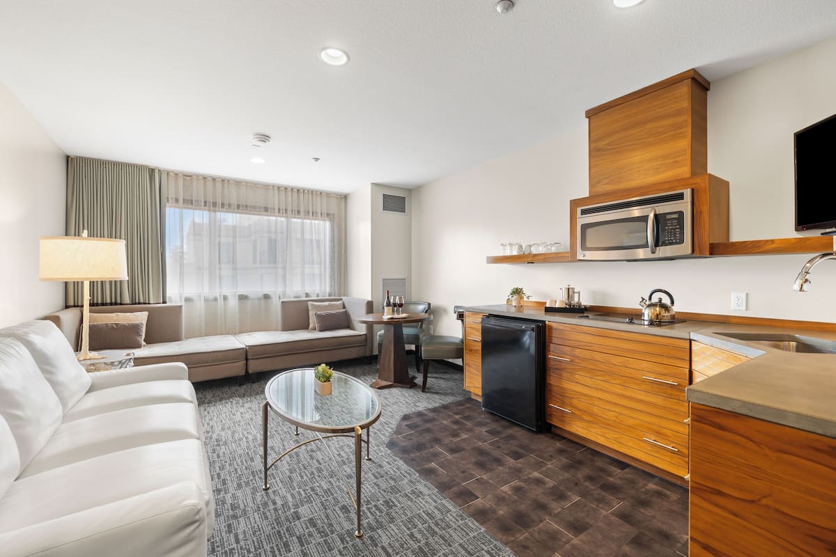 A modern living room with a sofa, a glass coffee table, and a kitchen area featuring a microwave and a refrigerator.