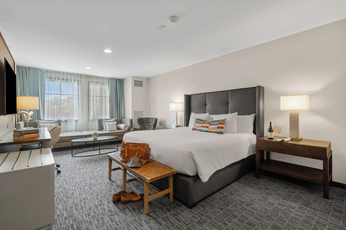 A hotel room with a large bed, bedside tables, a desk, a chair, and a sofa.
